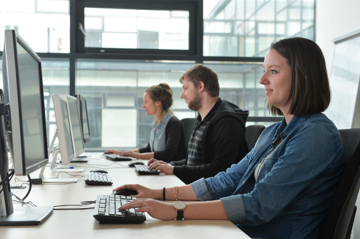 Drei junge Leute sitzen vor Bildschirmen und arbeiten