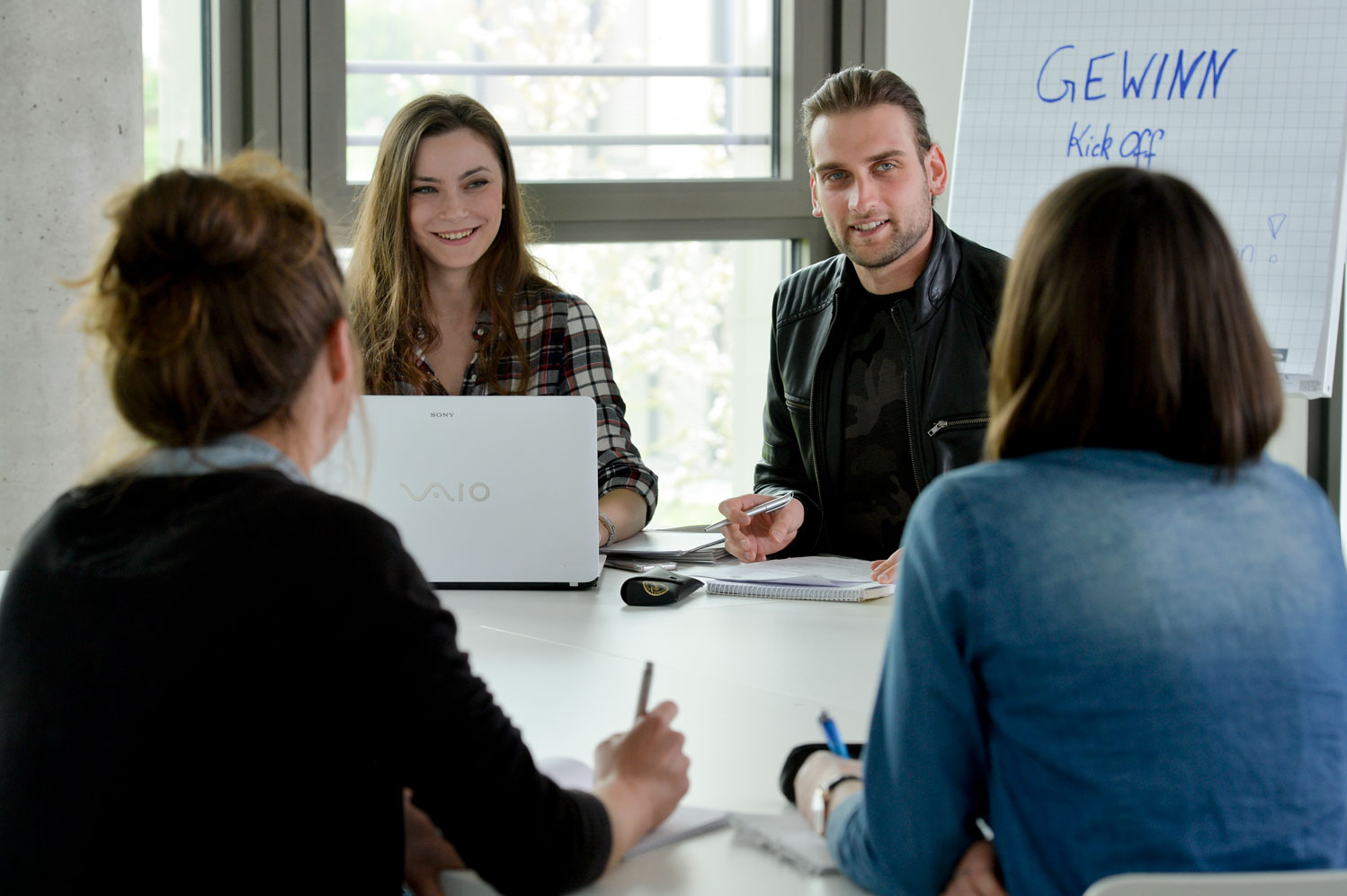 Drei Studentinnen und Studenten sitzen lernend an einem Tisch und sind miteinander im Gespräch