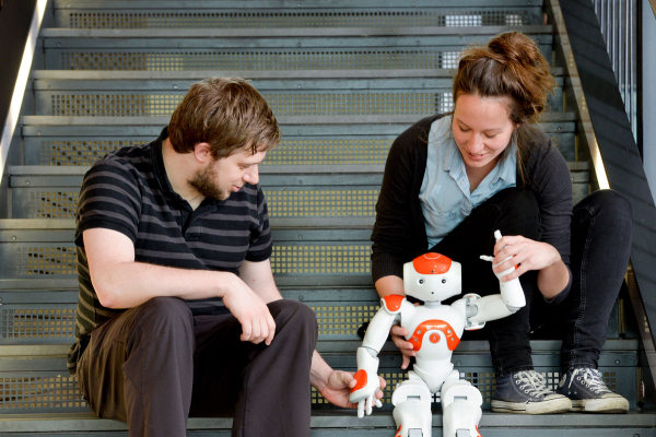 Ein Mann und eine Frau sitzen auf einer Treppe und betrachten einen Roboter