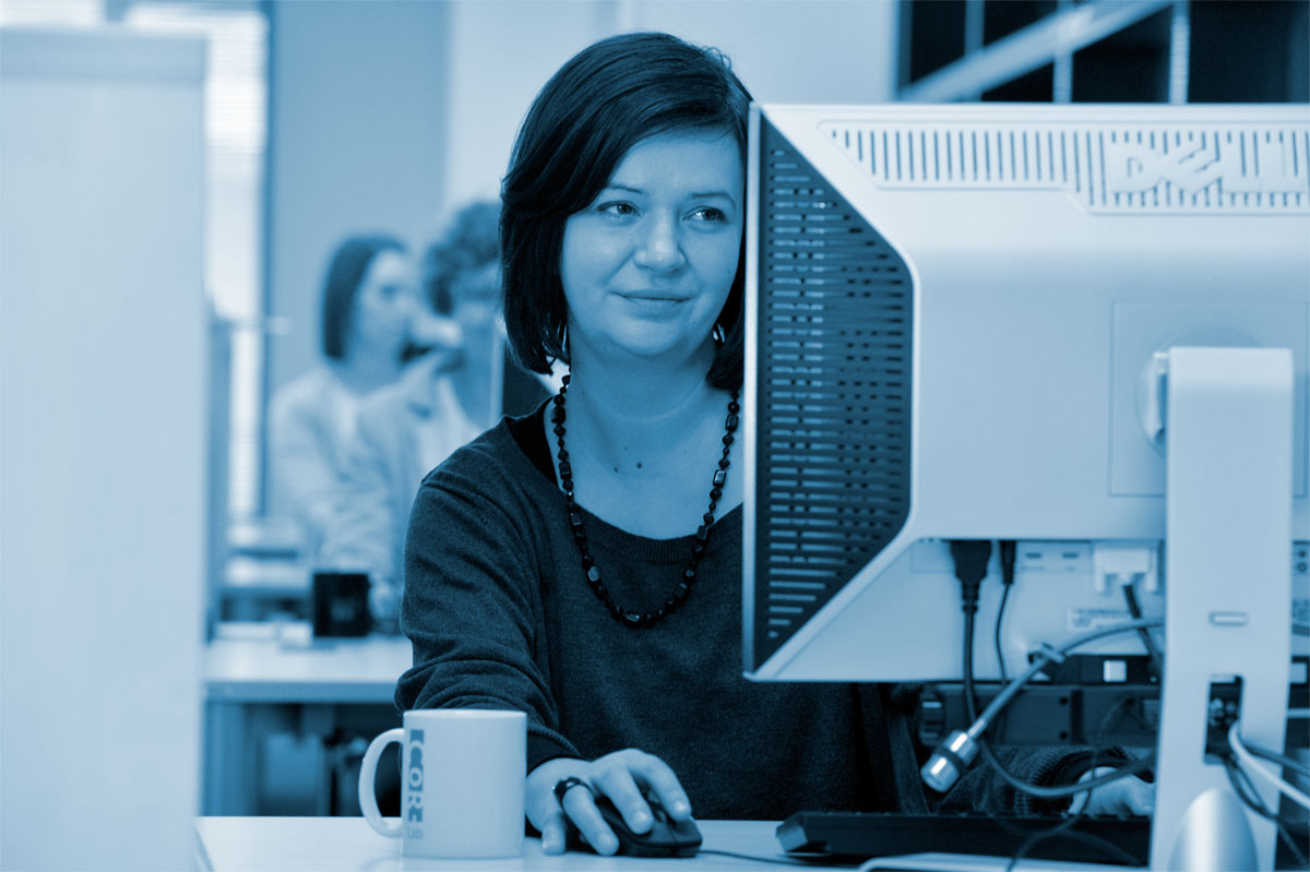 Frau sitzt am Schreibtisch und schaut auf einen Computerbildschirm.