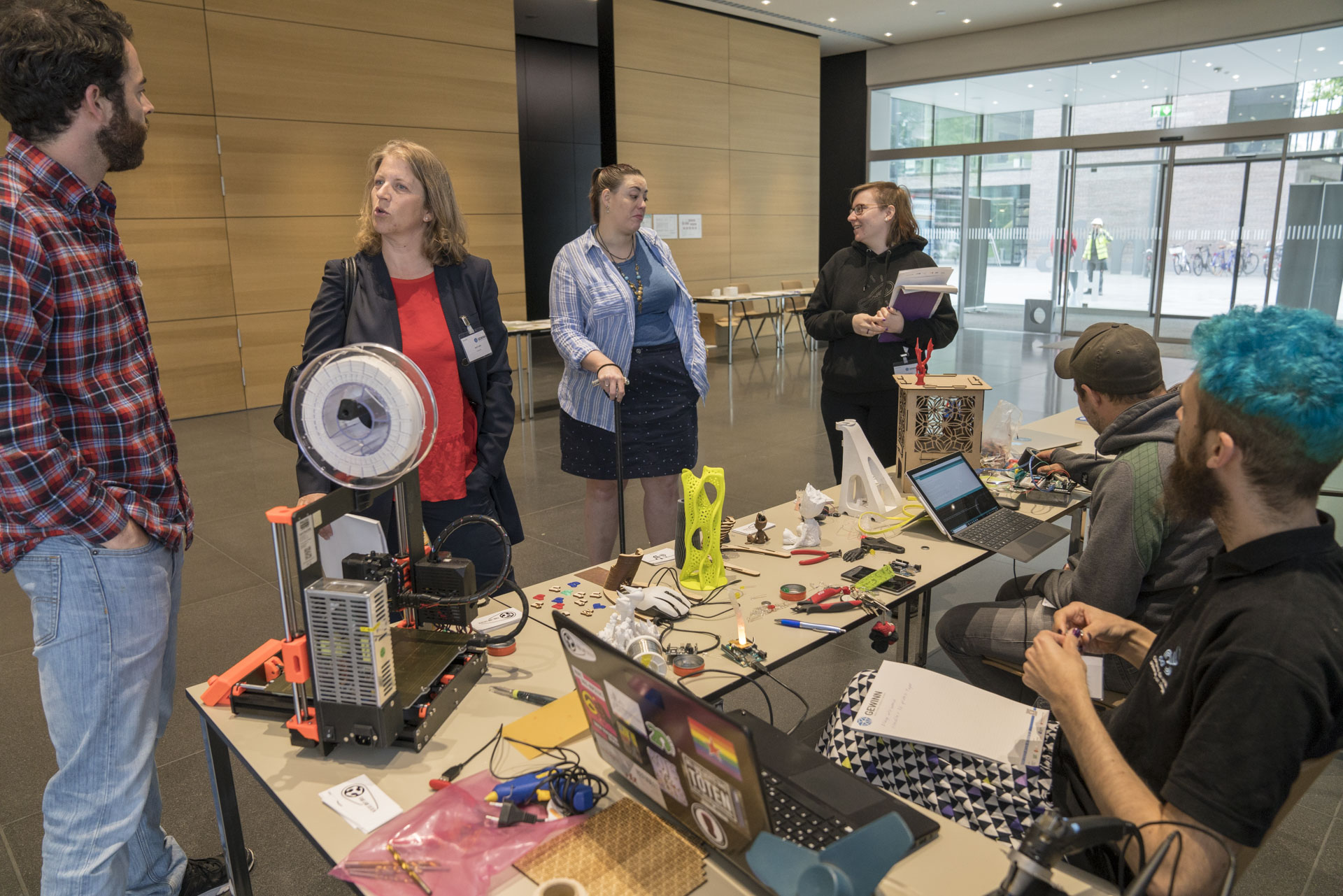 Vier Personen diskutieren vor dem Ausstellertisch des FabLab Siegen