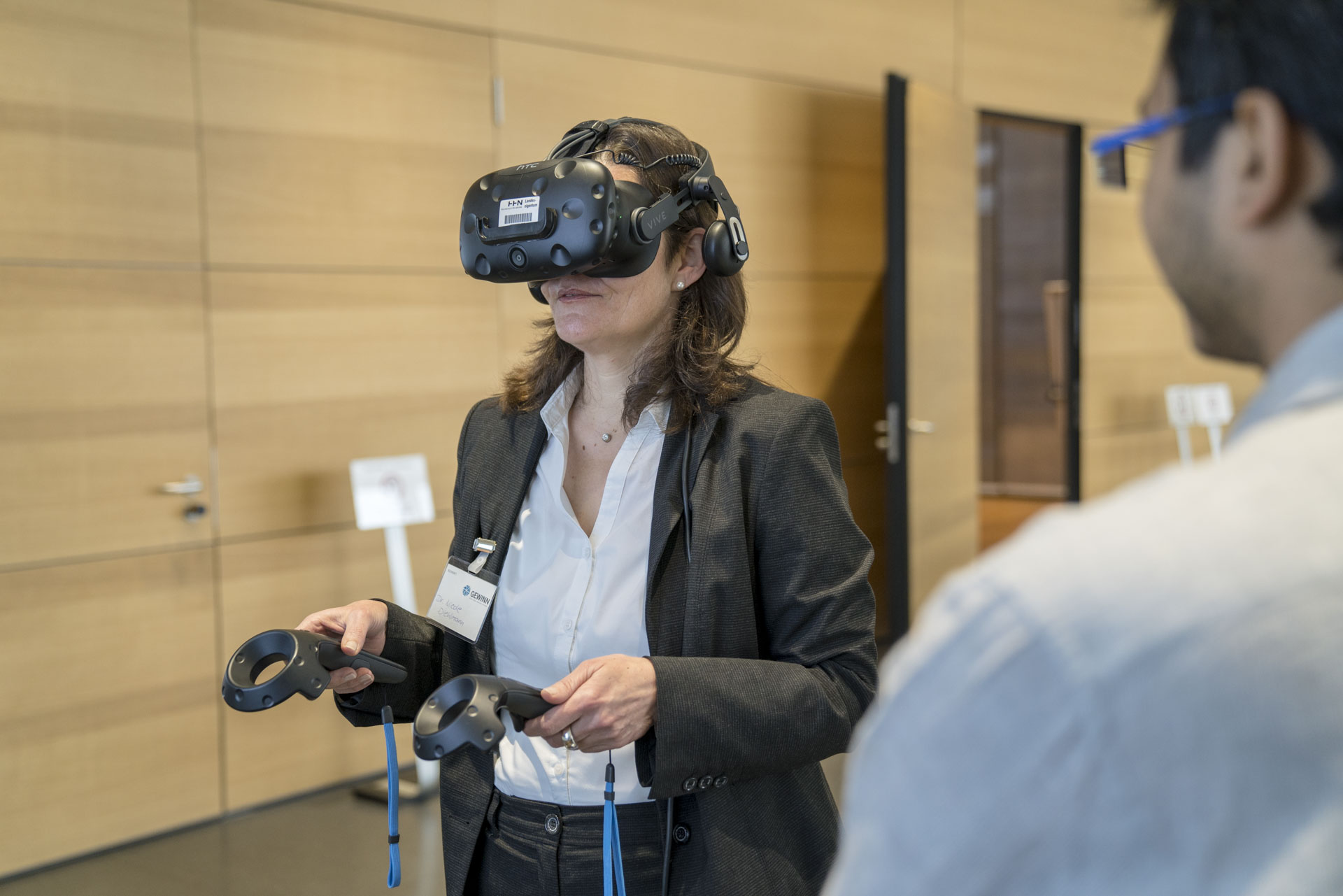 Frau mit VR-Brille, im Vordergrund Mann, der assistiert