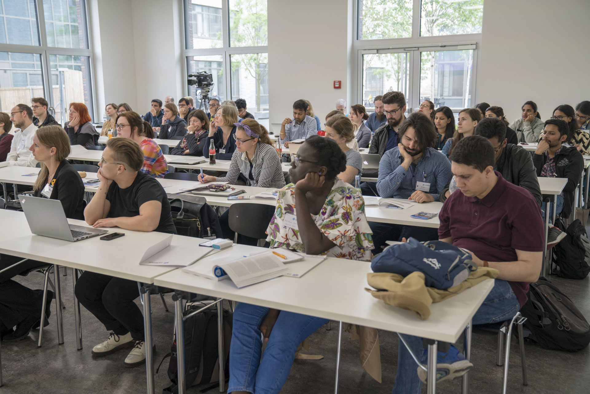 Zuhörer/innen an langen Tischen sitzend