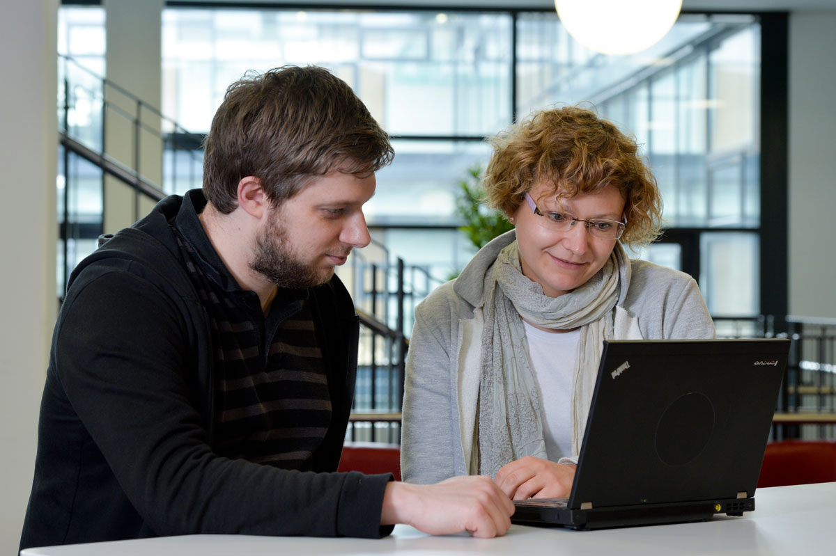Zwei Personen vor Laptop Ein Mann und eine Frau sitzen an einem Tisch und schauen gemeinsam auf den Bildschirm eines Laptops